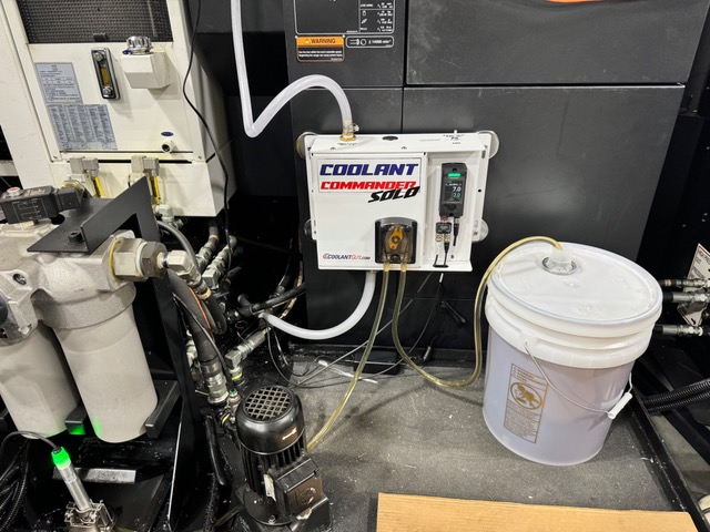 Coolant Commander SOLO installed on a CNC machine with a five-gallon concentrate pail beside it and refractometer reading 7.0 percent on target